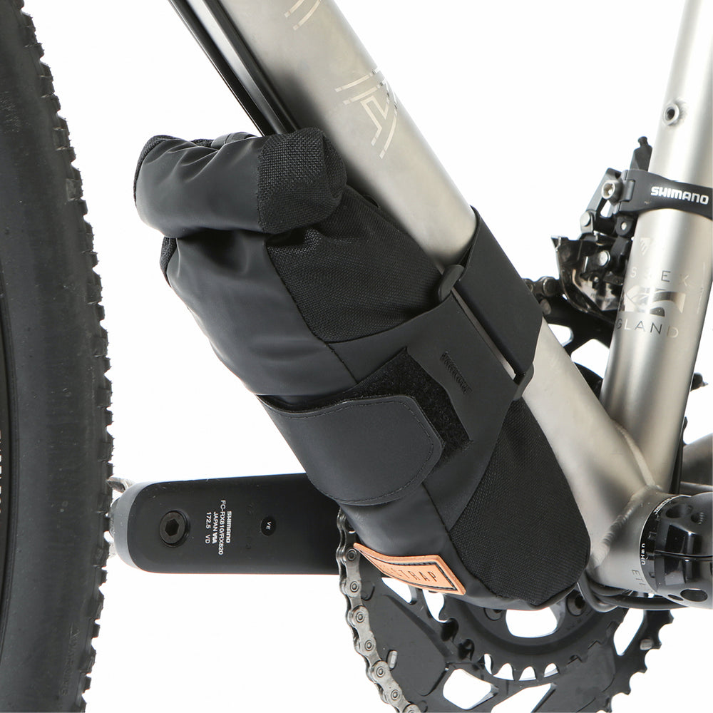 A black Restrap downtube bag attached to a bicycle frame beneath the downtube, featuring a roll-top closure and velcro strap.