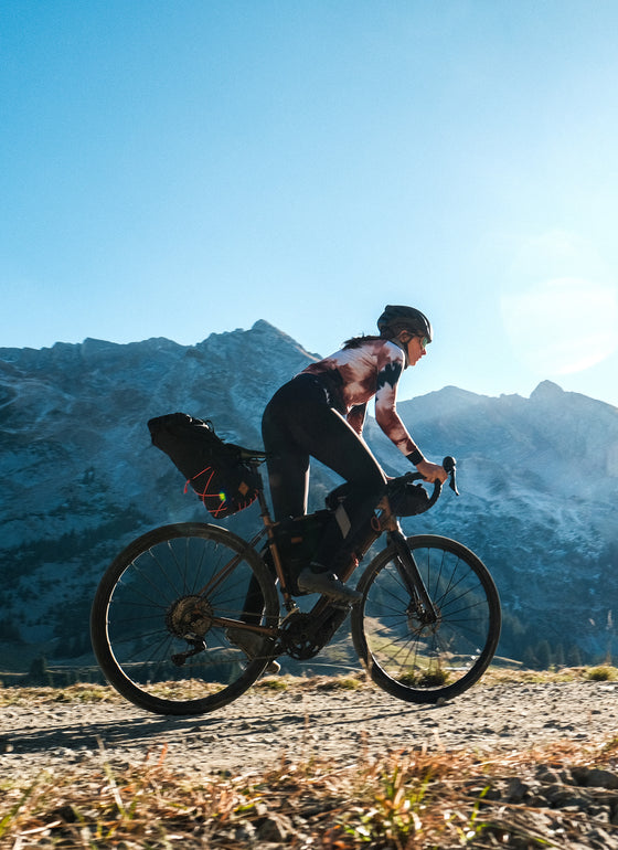 female rider in the mountains riding out of the saddle with restrap bags mounted to the bike