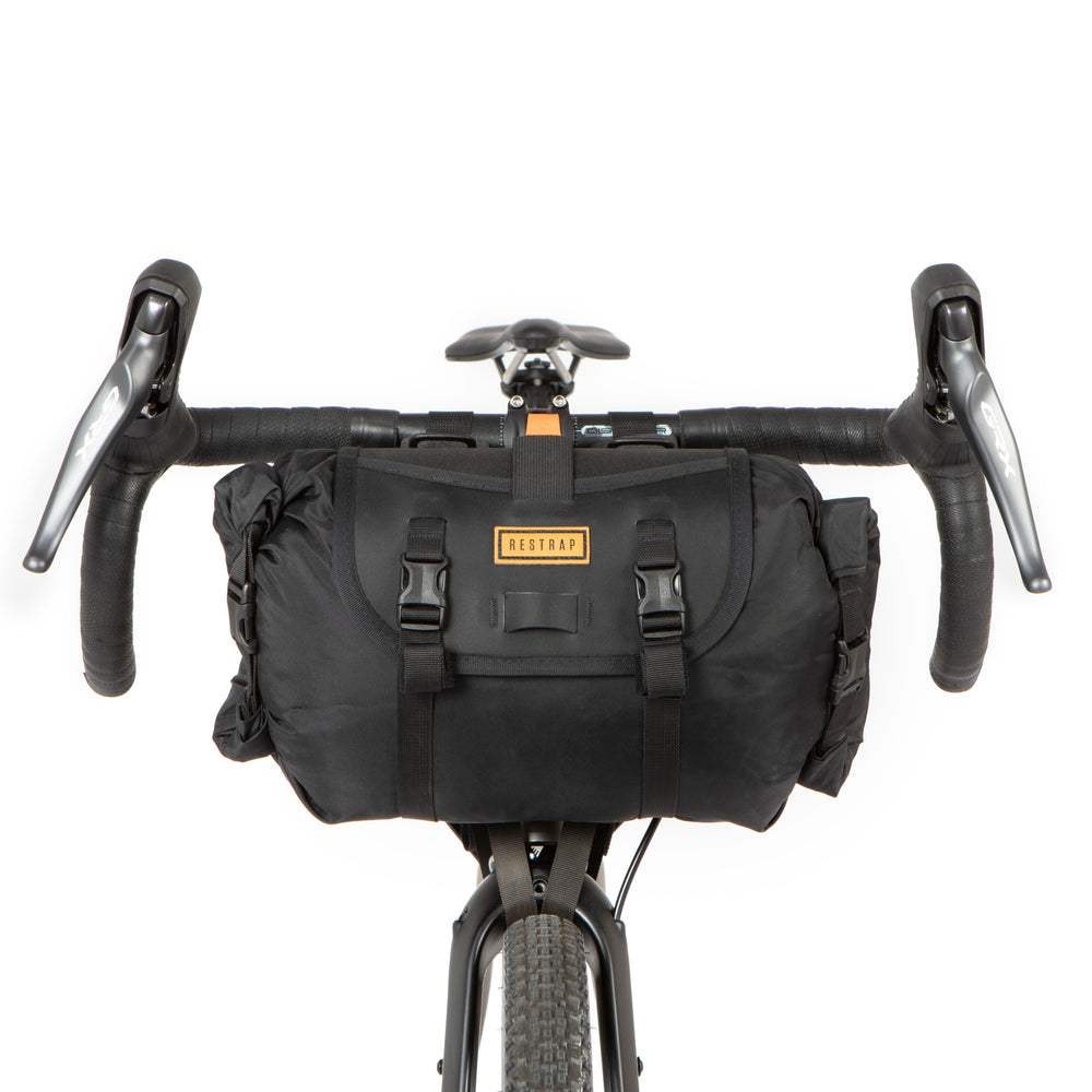 A black Restrap Holster Bar Bag mounted on a bicycle handlebar in front of a white background