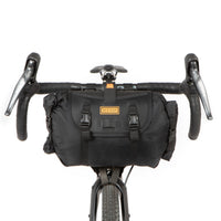 A black Restrap Holster Bar Bag mounted on a bicycle handlebar in front of a white background