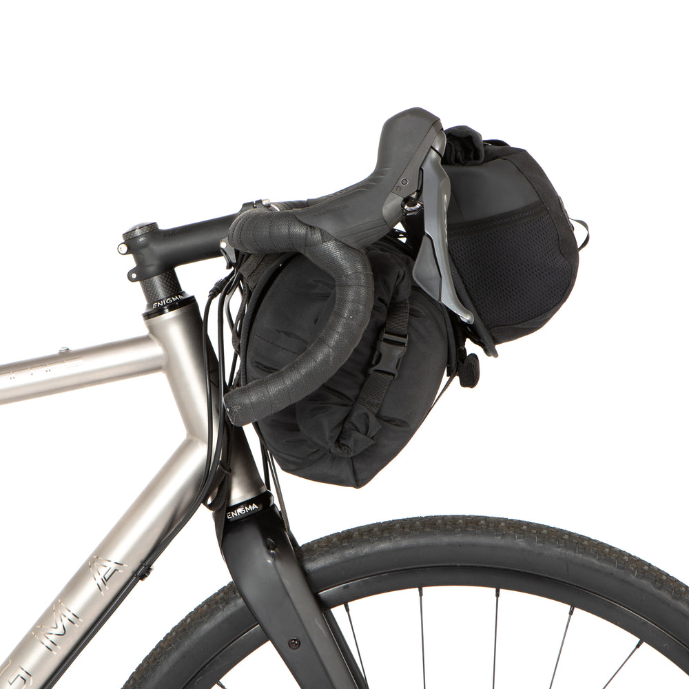 A black Restrap Holster Bar Bag Plus mounted on a bicycle handlebar, featuring a rolltop canister bag attached in front, pictured from the side