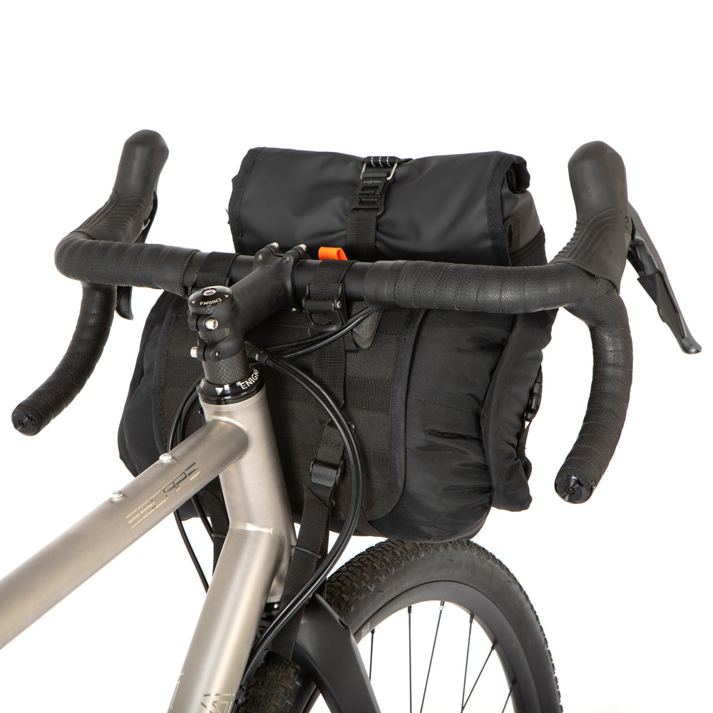 A black Restrap Holster Bar Bag Plus mounted on a bicycle handlebar, featuring a rolltop canister bag attached in front, shown from behind