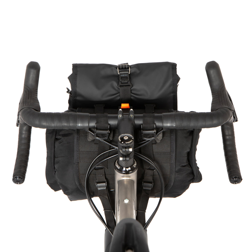 A black Restrap Holster Bar Bag Plus mounted on a bicycle handlebar, featuring a rolltop canister bag attached in front, shown from behind and above