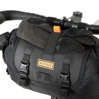 A close up of restrap holster bar bag attached to the handlebars of a bicycle, designed for bikepacking.