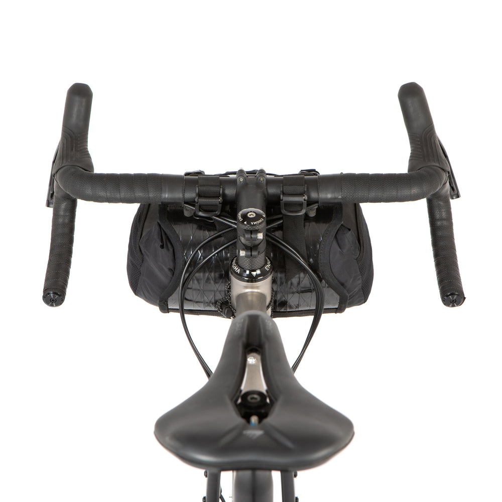 A black Race Bar Bag attached to the handlebars of a bicycle, featuring a holster system and a roll-top dry bag - this is attached to drop handlebars