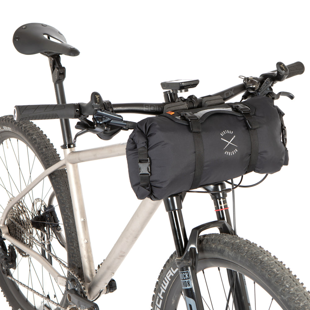 A black Race Bar Bag attached to the handlebars of a bicycle, featuring a holster system and a roll-top dry bag - this is attached to flat handlebars on a mountain bike