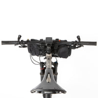 A black Race Bar Bag attached to the handlebars of a bicycle, featuring a holster system and a roll-top dry bag - this is attached to flat handlebars on a mountain bike