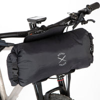 A black Race Bar Bag attached to the handlebars of a bicycle, featuring a holster system and a roll-top dry bag - this is attached to flat handlebars on a mountain bike. The dry bag is being removed from the holster