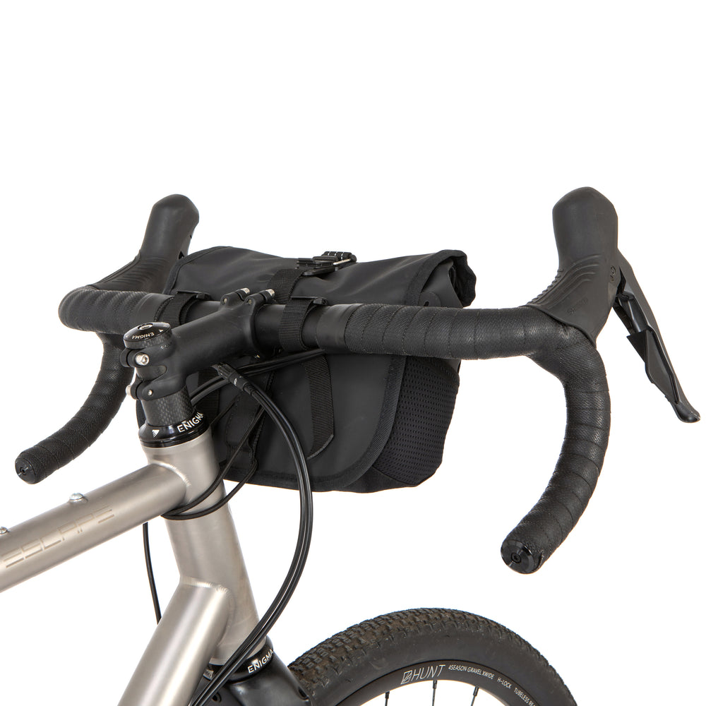 A black Rolltop Canister Bag attached to the handlebars of a bicycle, shown from the rear