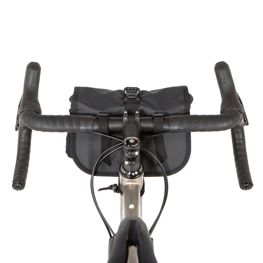 A black Rolltop Canister Bag attached to the handlebars of a bicycle, shown from a riders perspective