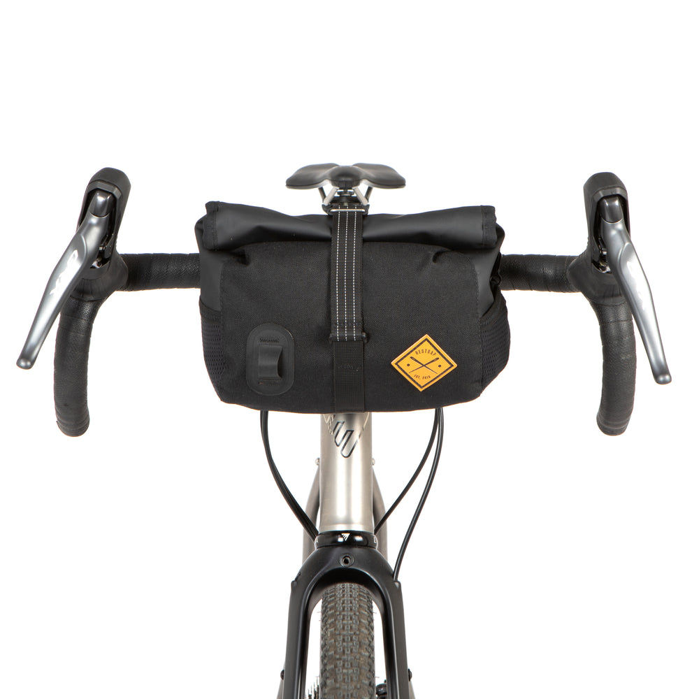 A black Rolltop Canister Bag attached to the handlebars of a bicycle, featuring a waterproof design with a capacity of 4L and a Fidlock buckle.