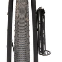 A black laser cut aluminium cargo cage mounted to the fork of a bicycle, with Restrap branded rubber label visible, shown from profile view