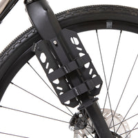 A black laser cut aluminium cargo cage mounted to the fork of a bicycle, with Restrap branded rubber label visible and fast straps attached