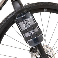 A black laser cut aluminium cargo cage mounted to the fork of a bicycle, with nalgene bottle attached