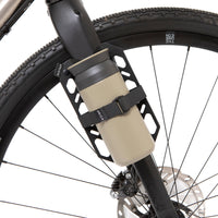 A black laser cut aluminium cargo cage mounted to the fork of a bicycle, with Restrap branded rubber label visible and coffee cup attached