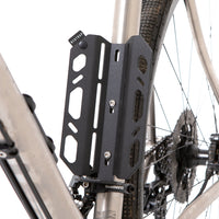 A black laser cut aluminium cargo cage mounted to the seat tube of a bicycle, with Restrap branded rubber label visible.