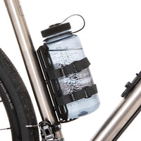 A black laser cut aluminium cargo cage mounted to the seat tube of a bicycle, with Restrap branded rubber label visible.
