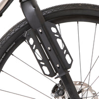 A black laser cut aluminium cargo cage mounted to the fork of a bicycle, with Restrap branded rubber label visible.
