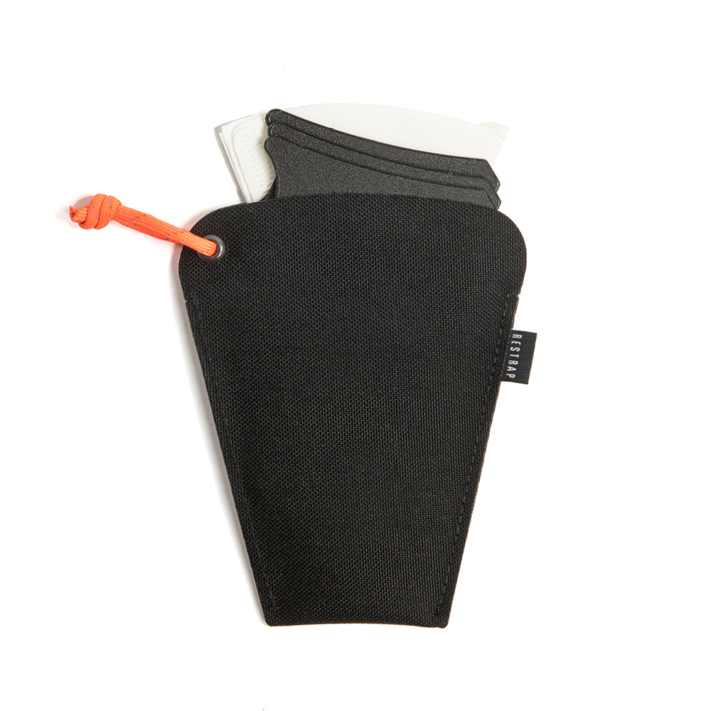 A black portable coffee dripper disassembled into three pieces, alongside an orange filter clip and a white V60 coffee filter, all placed on a white background.