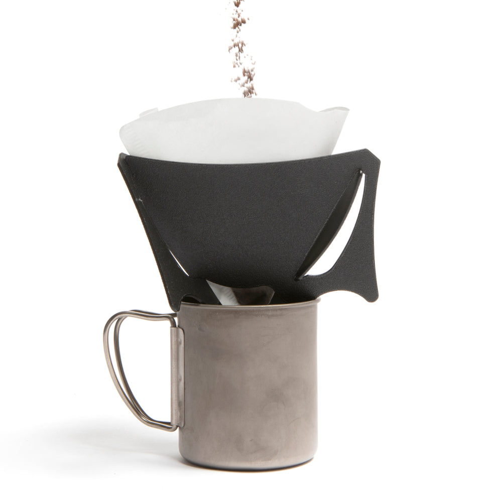 A black portable coffee dripper, with coffee being added to it, with V60 filter inside