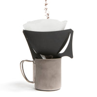A black portable coffee dripper, with coffee being added to it, with V60 filter inside