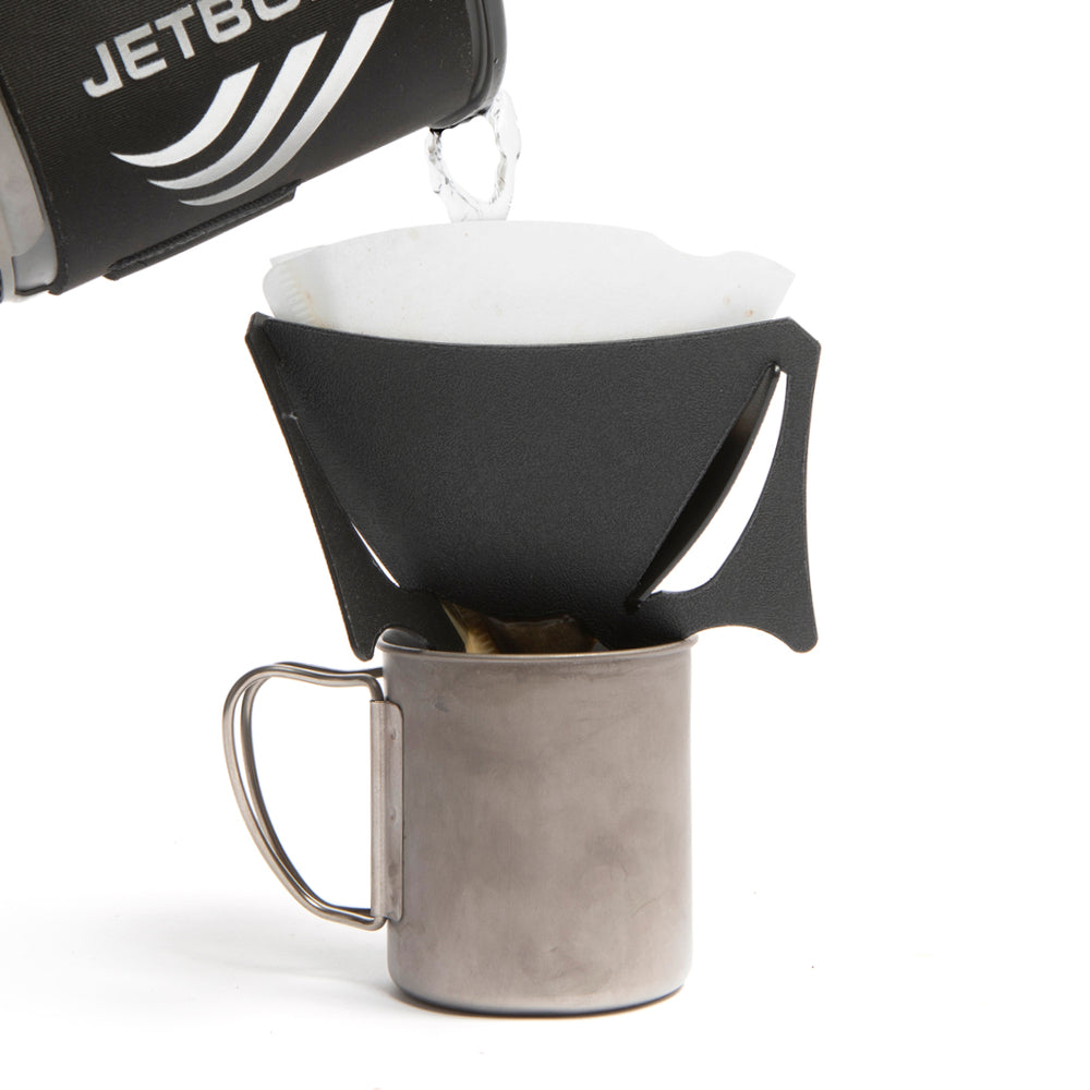 A black portable coffee dripper, with coffee being added to it, with V60 filter inside