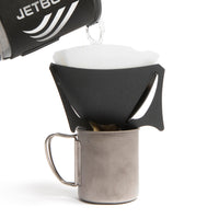 A black portable coffee dripper, with coffee being added to it, with V60 filter inside