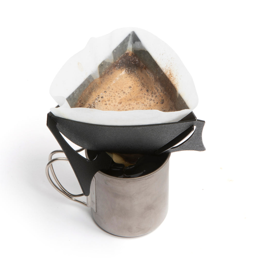 A black portable coffee dripper, with coffee being added to it, with V60 filter inside