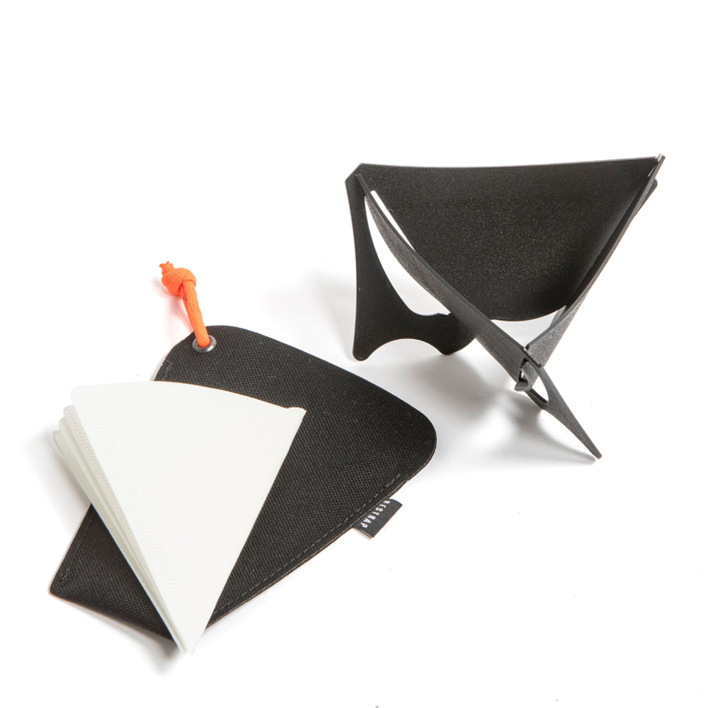A black portable coffee dripper disassembled into three pieces, alongside an orange filter clip and a white V60 coffee filter, all placed on a white background.