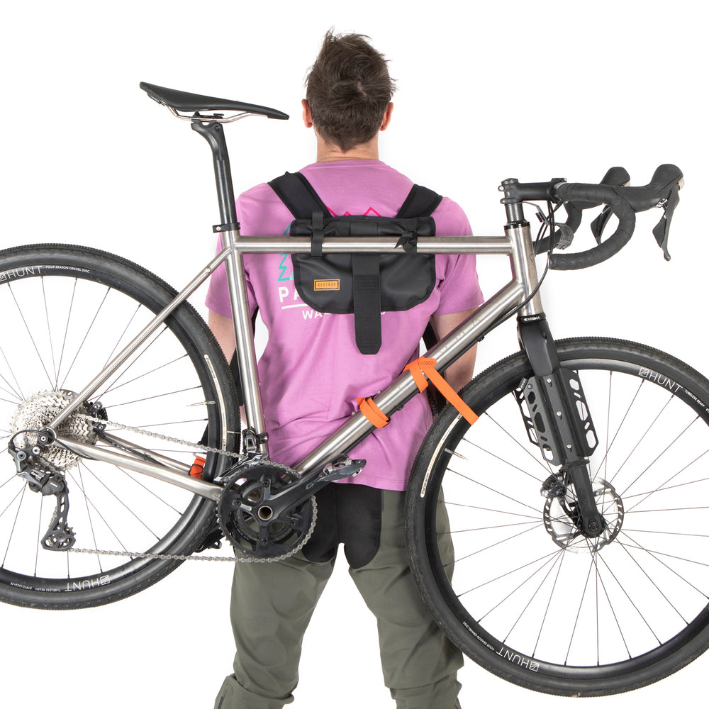 A black hike a bike harness attached to the frame of a bicycle, designed for carrying the bike on one's back.