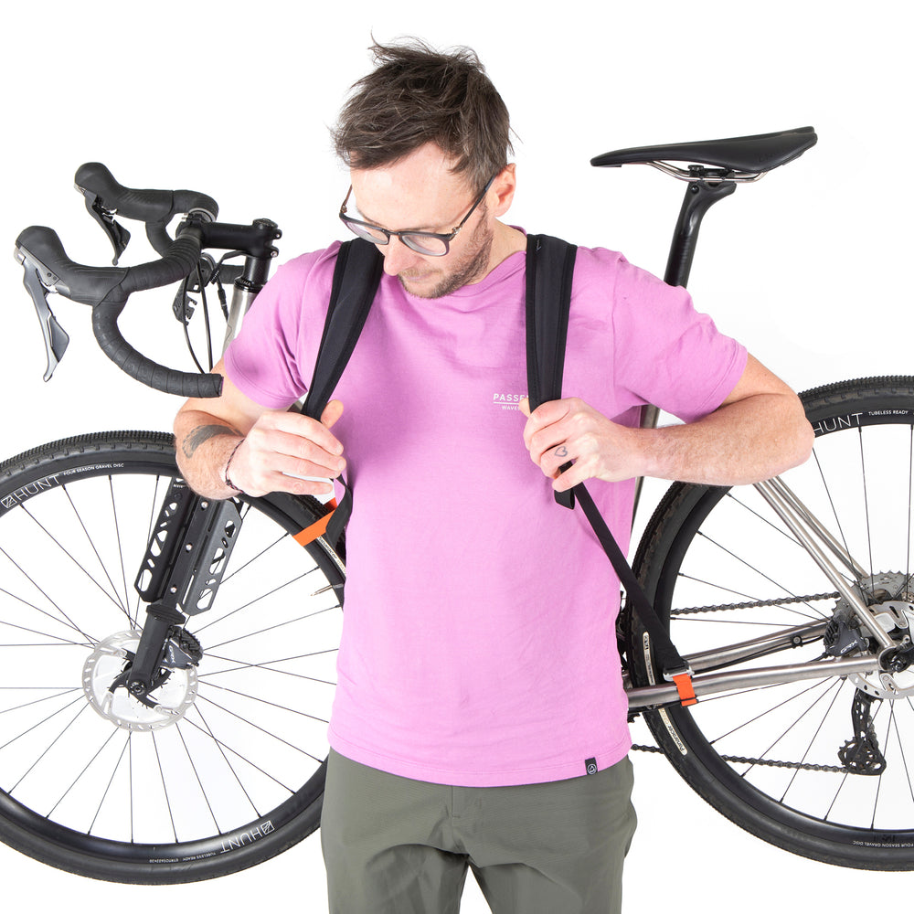 A black hike a bike harness attached to the frame of a bicycle, designed for carrying the bike on one's back.