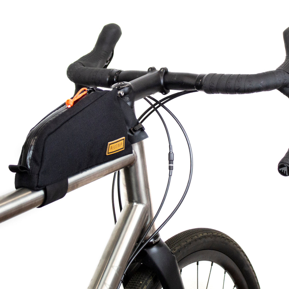 A black Restrap top tube bag attached to the frame of a bicycle, designed to hold tools and snacks within reach.