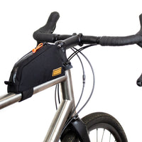 A black Restrap top tube bag attached to the frame of a bicycle, designed to hold tools and snacks within reach.