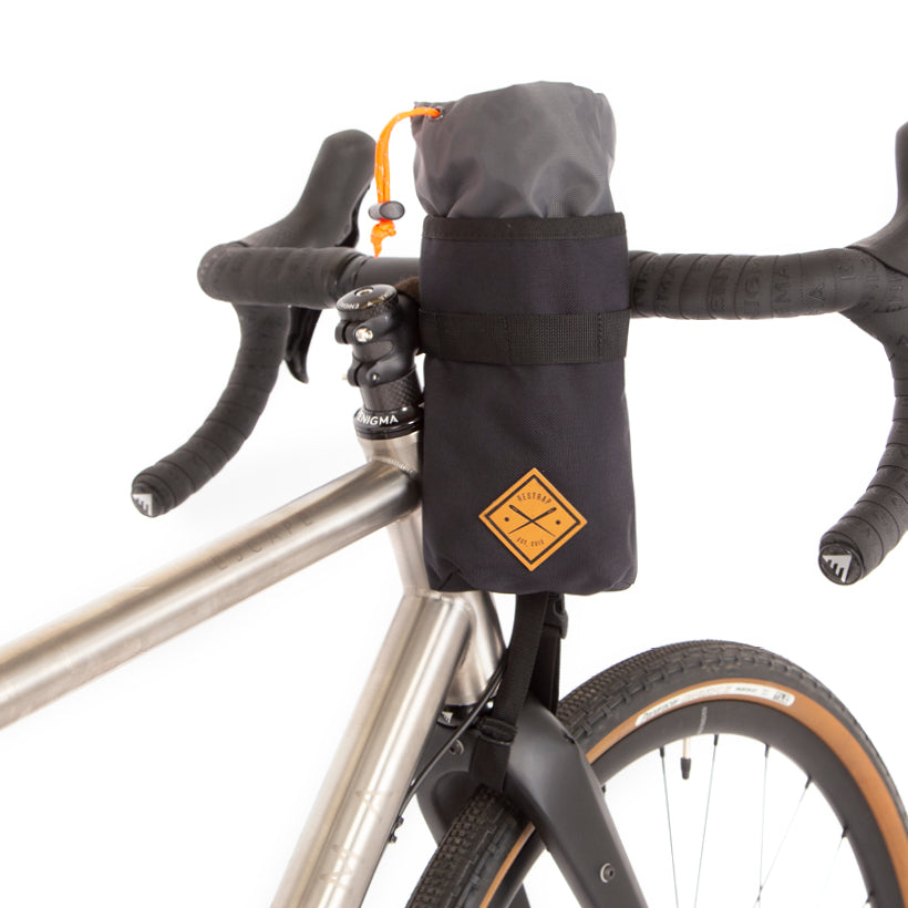 A black Restrap stem bag mounted on the handlebar of a bicycle, designed for carrying a water bottle or other items, with an orange drawstring and the Restrap logo in yellow.