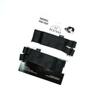 A black Restrap horizontal pedal strap fitted onto it's packaging, with visible nylon webbing and metal buckle.