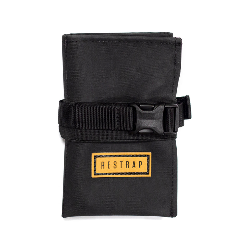 A black Restrap tool roll with a visible brand label, designed to be attached to a bicycle saddle or kept in a jersey pocket.