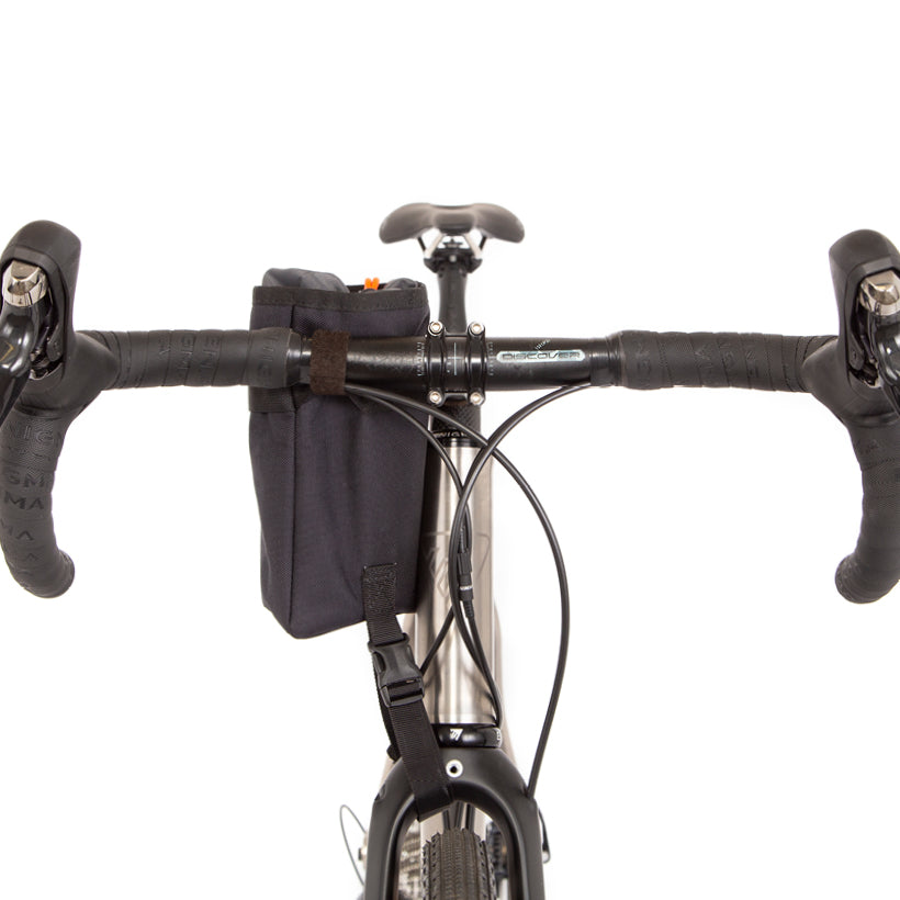 A black Restrap stem bag mounted on the handlebar of a bicycle, shown from the front
