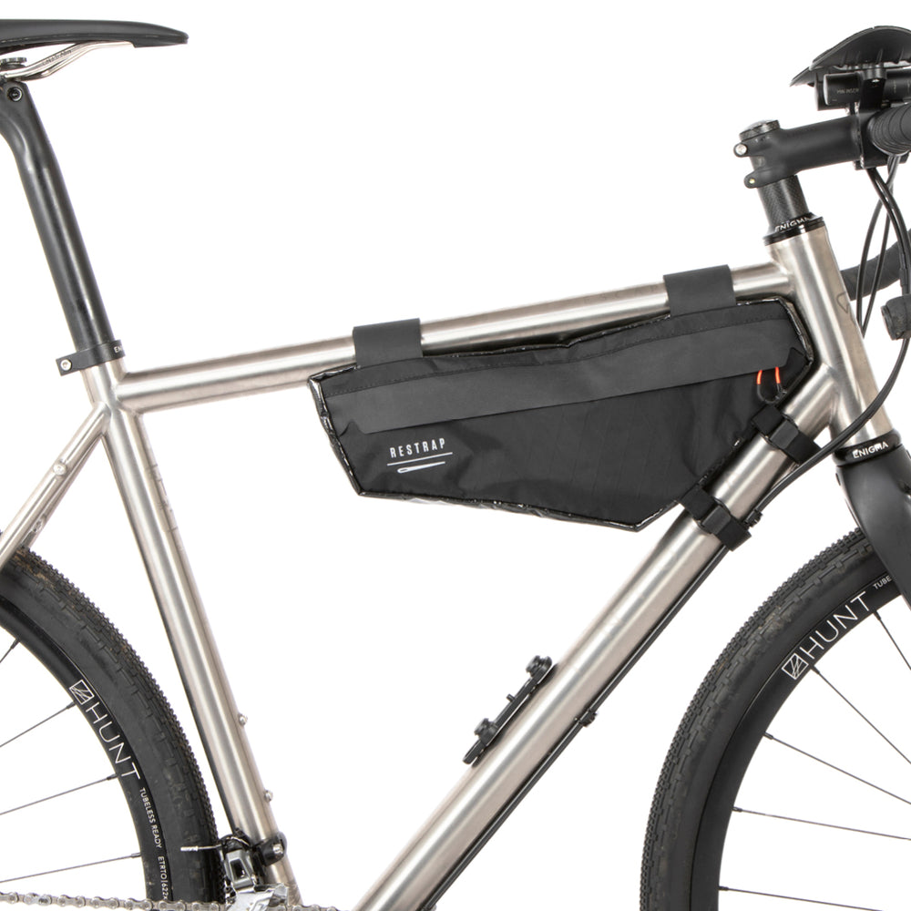A small black race frame bag attached to the frame of a bicycle, designed for bikepacking.
