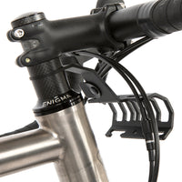 A black metal bumper bar mounted on a bicycle handlebar designed for spacing a handlebar bag further outwards and upwards