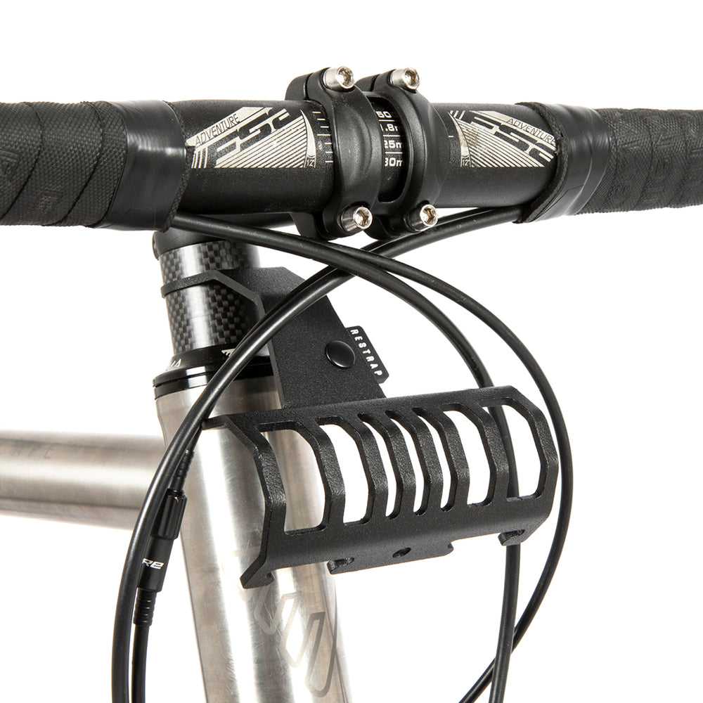 A black metal bumper bar mounted on a bicycle handlebar designed for spacing a handlebar bag further outwards and upwards