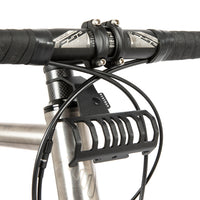 A black metal bumper bar mounted on a bicycle handlebar designed for spacing a handlebar bag further outwards and upwards