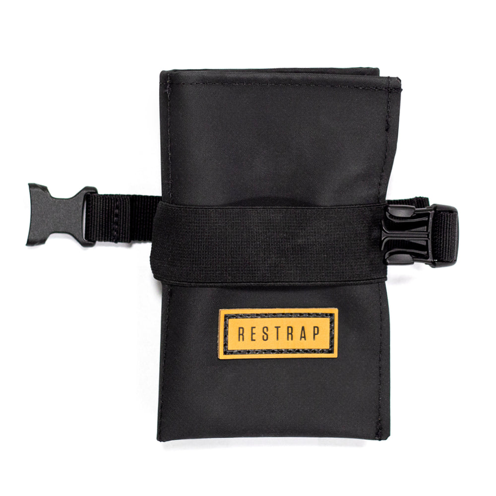 A black Restrap tool roll with a visible brand label, designed to be attached to a bicycle saddle or kept in a jersey pocket.