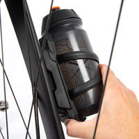 Person holding a black bicycle water bottle holder with a water bottle against a white background
