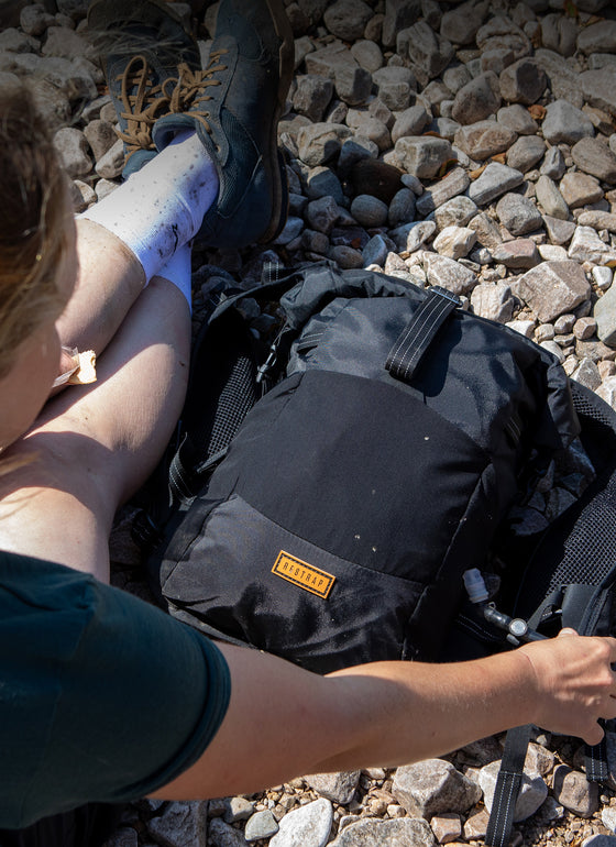 woman sat on a pebble beach with a restrap rolltop hydration vest