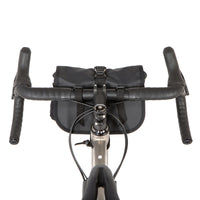 A black Rolltop Canister Bag attached to the handlebars of a bicycle, shown from a riders perspective